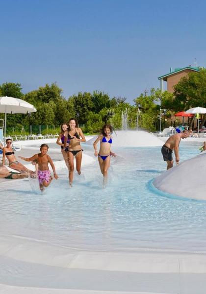 Famiglie si divertono in piscina con fontane e lettini.