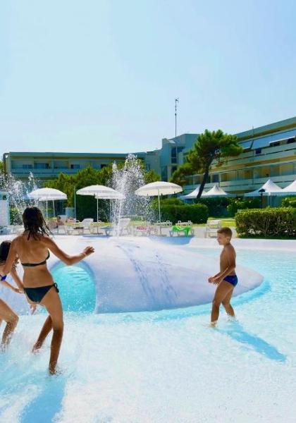 Kinder spielen im Pool mit Brunnen, unter der Sonne.