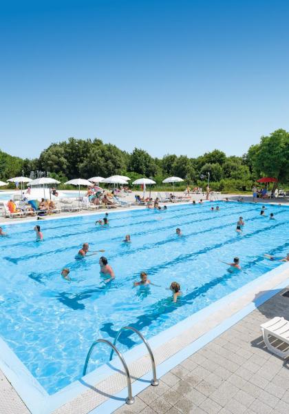 Crowded outdoor pool with umbrellas and sunbeds.