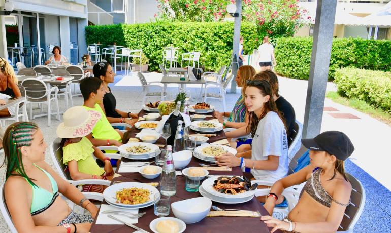 Famiglia e amici pranzano insieme all'aperto in una giornata soleggiata.