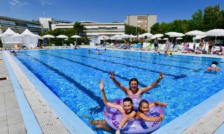 Persone si divertono in una piscina all'aperto con lettini e ombrelloni.