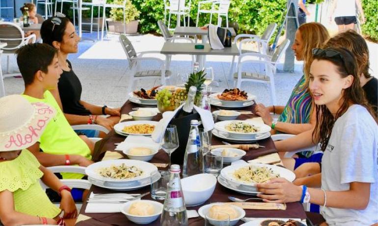 Famiglia a pranzo all'aperto con piatti di pasta e frutti di mare.