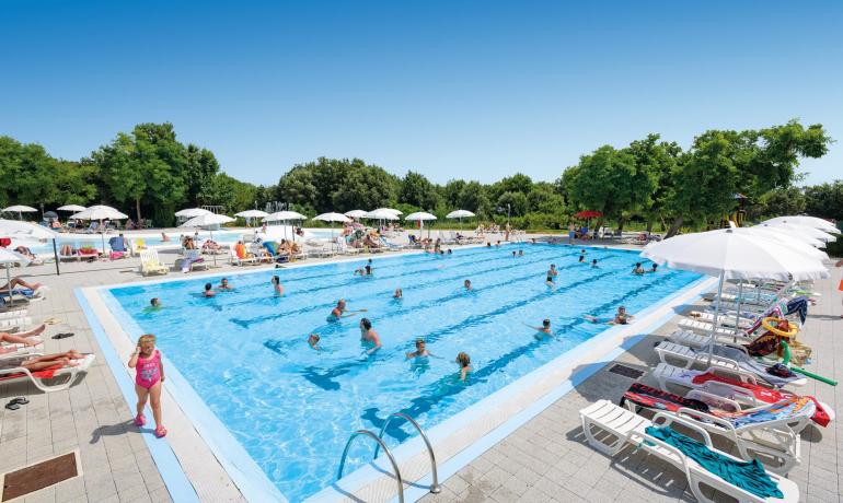 Crowded outdoor pool with umbrellas and sunbeds.